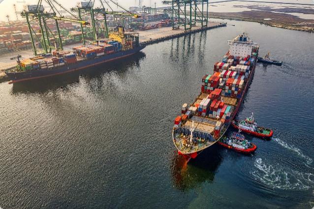 Container ship being guided into a port by tugs